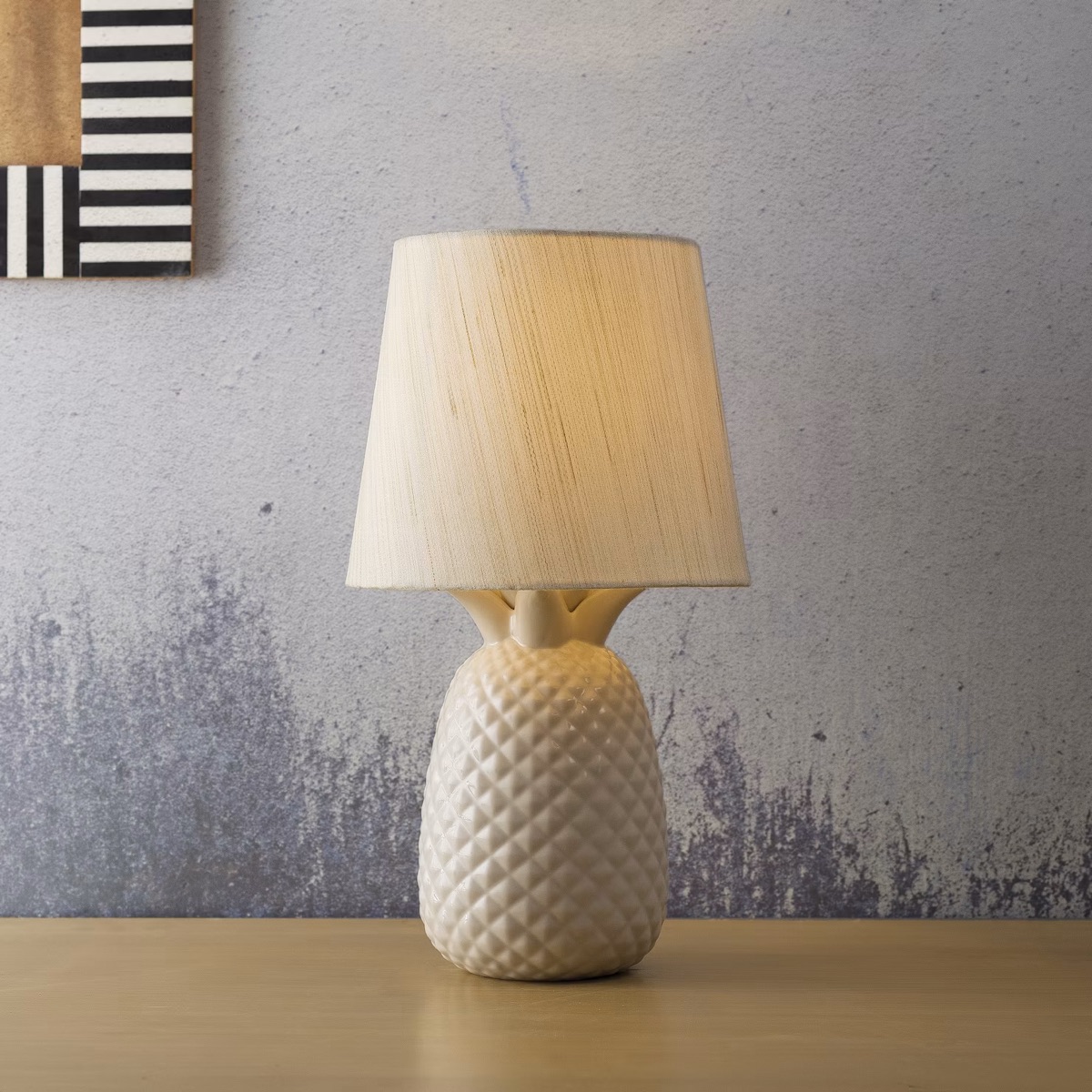 A white ceramic table lamp, lit, on a wooden surface.